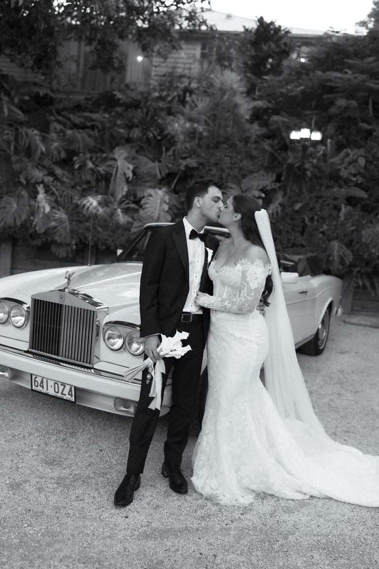 A bride and groom together beside a vintage car